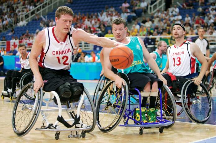 A male wheelchair basketball player is dribbling the ball