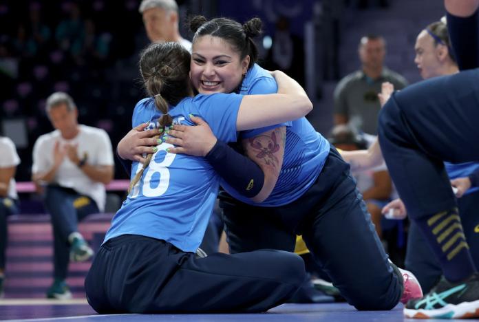 Two female sitting volleyball players hug on the court