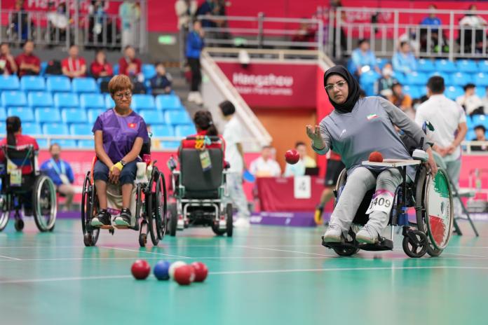 A female boccia athlete is throwing a ball during a competition