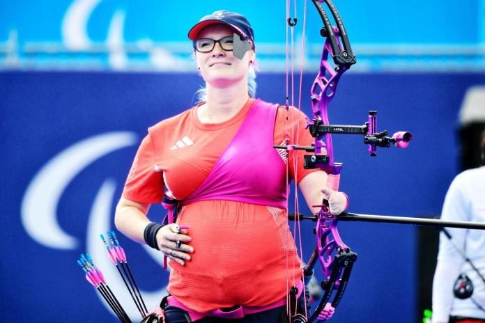 A female Para archer, who is seventh month pregnant, is smiling while touching her stomach