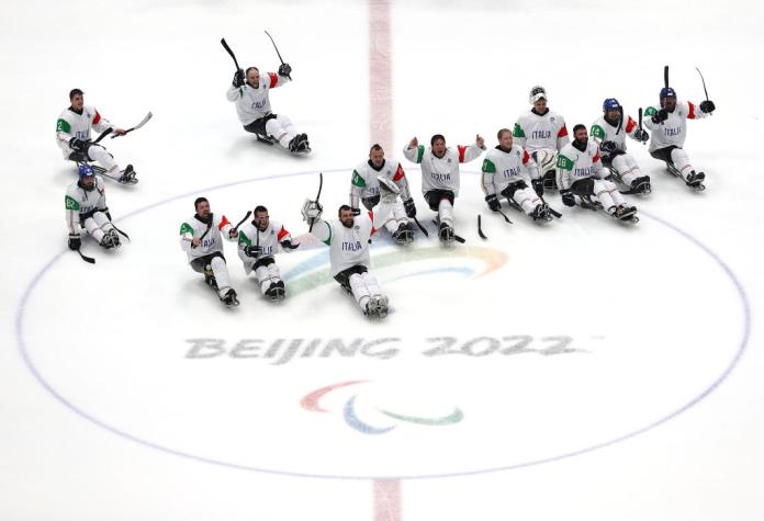 Twelve male Para ice hockey players on the ice, celebrating and posing for a photograph