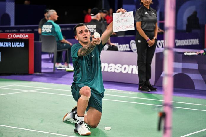 A male athlete gets down on his knee and holds a sign that says "Edwarda aceita casar conmigo?"