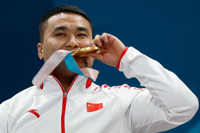A male athlete poses for a photograph, he is kissing a gold medal he is holding with his left hand