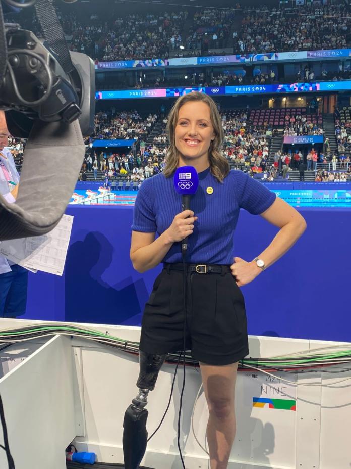 Ellie Cole, a retired Para swimmer, holds a mic and poses in front of a camera at the Paris 2024 swimming venue
