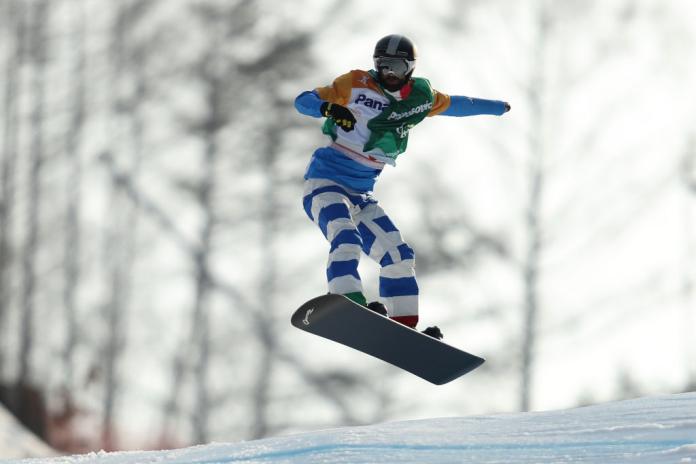 A male Para snowboarder makes a jump during a Para snowboard competition