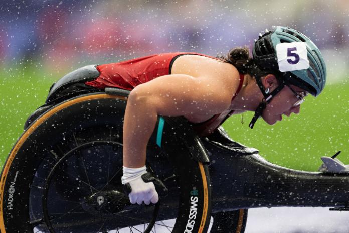 A female wheelchair racer is racing, the photo is taken from the side.