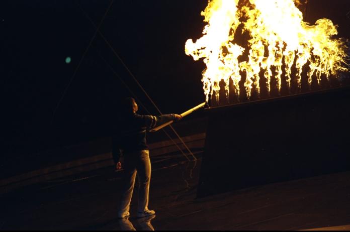 A person is holding a torch and lighting the Nagano 1998 Paralympic Winter Games flame.