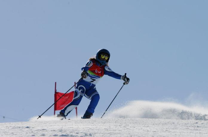 Silvia Parente is competing in Para alpine skiing at the Torino 2006 Paralympic Winter Games. She is wearing a head gear with an illustration of yellow eyes