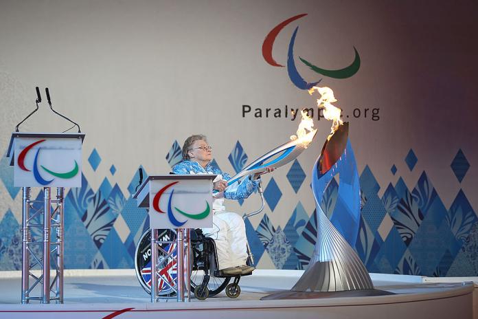 Paralympian Caz Walton is holding a torch in front of a silver cauldron