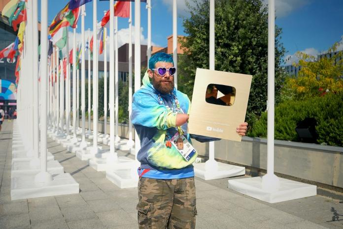 A male athlete wearing purple heart-shaped sunglasses holds YouTube's golden plaque