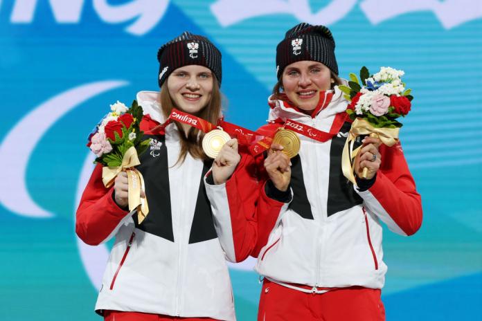 Two female athletes posing for a picture on the podium after receiving gold medals