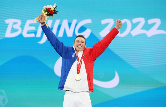 A male alpine skier raises both hands on the podium