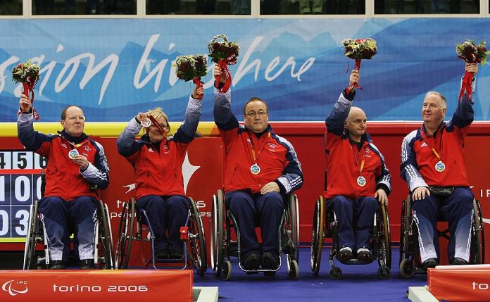 Five male and female athletes pose for a photo on the podium. They are holding flower bouquets.