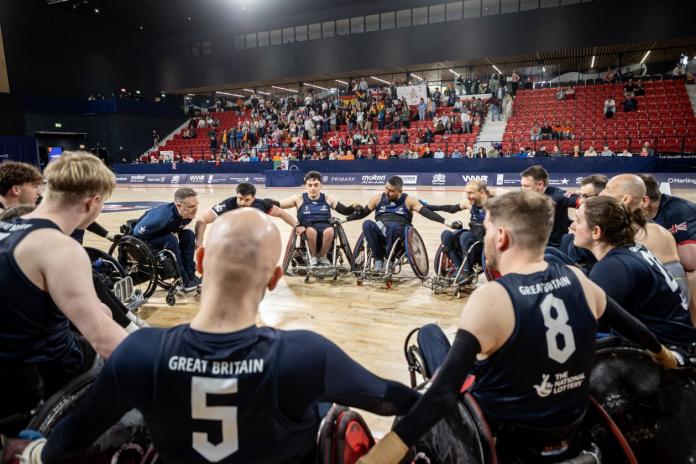 About 15 wheelchair rugby players of the Great Britain team form a circle on court.