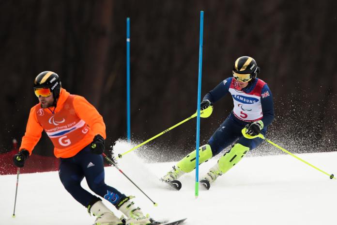 A female Para alpine skiing athlete is competing behind her sighted guide