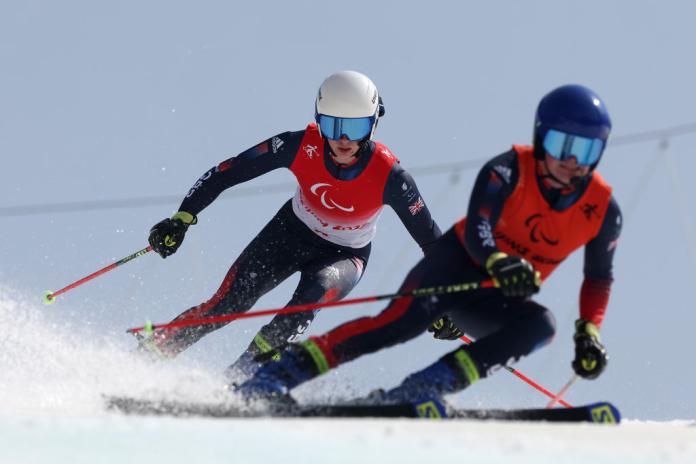 A male Para alpine skier is competing behind his guide
