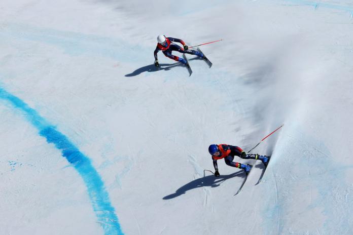 A male Para alpine skier is competing behind his guide