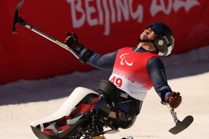 A male Para alpine skier opens his arms wide as he reacts after a race