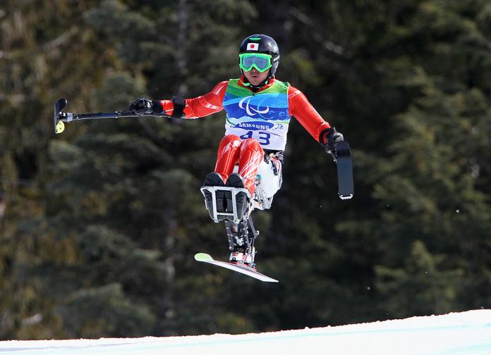A male athlete in a sit-skiing competition, he is in the air