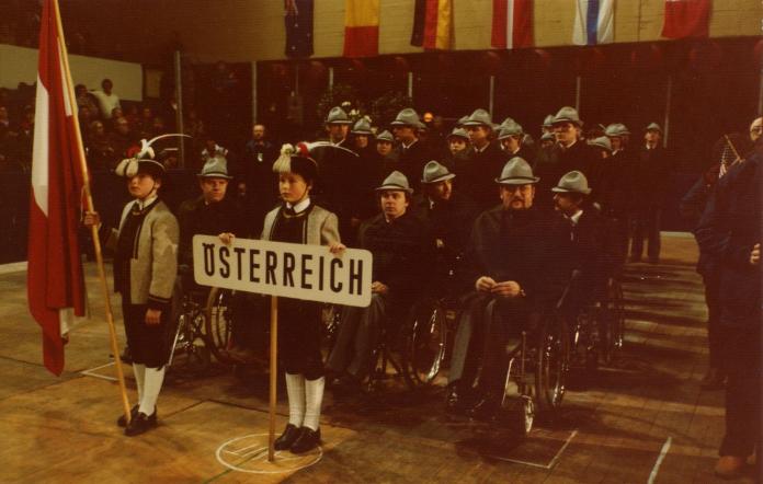 A group of Para athletes are lined up behind two children holding the Austrian flag and a banner that says Austria