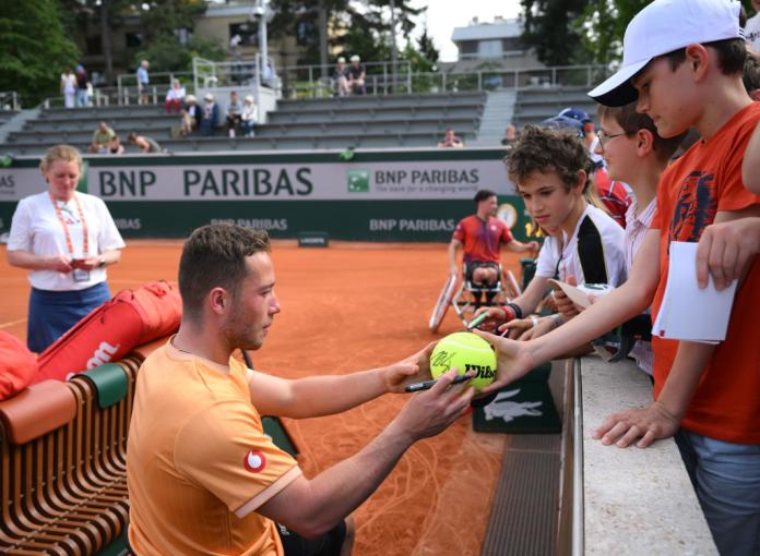A male wheelchair tennis player makes autographs for kids 