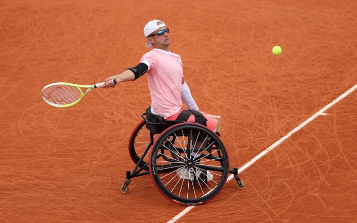 A male quad tennis player returns a ball on red clay court