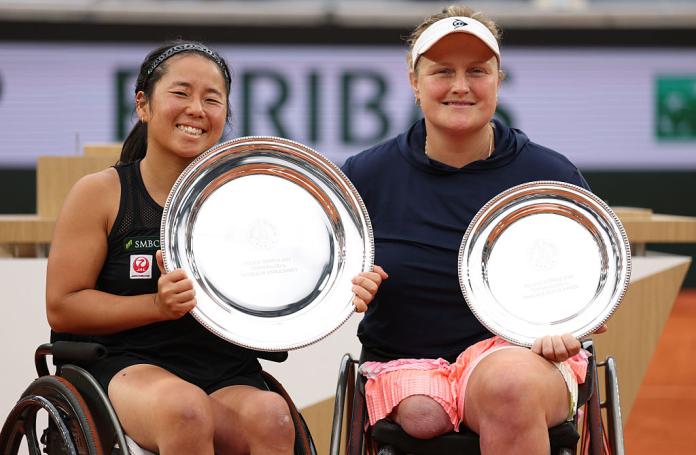 Two female whelehciar tennis players pose for a photo with silver trophies