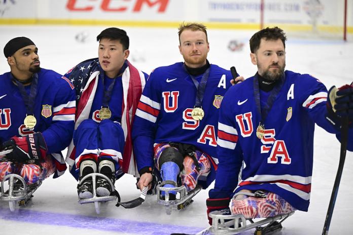 Four male Para ice hockey athletes are on the ice, wearing gold medals around their necks