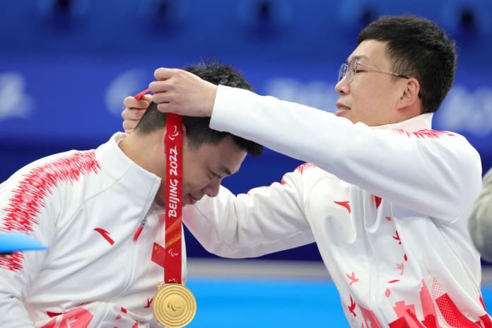 A male athlete puts a gold medal around his teammate's neck