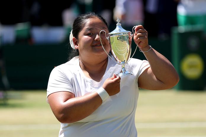 A female athlete wearing a white T-shirt is posing for a photo with a silver trophy 