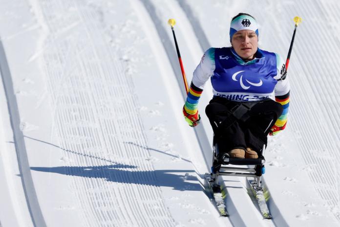 A female sit-skiing athlete is racing down hill in the cross-country segment of a Para biathlon event