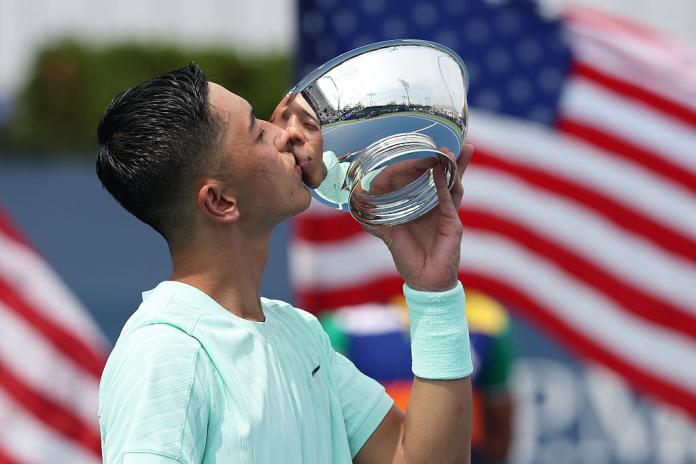A male wheelchair tennis player is kissing a silver trophy