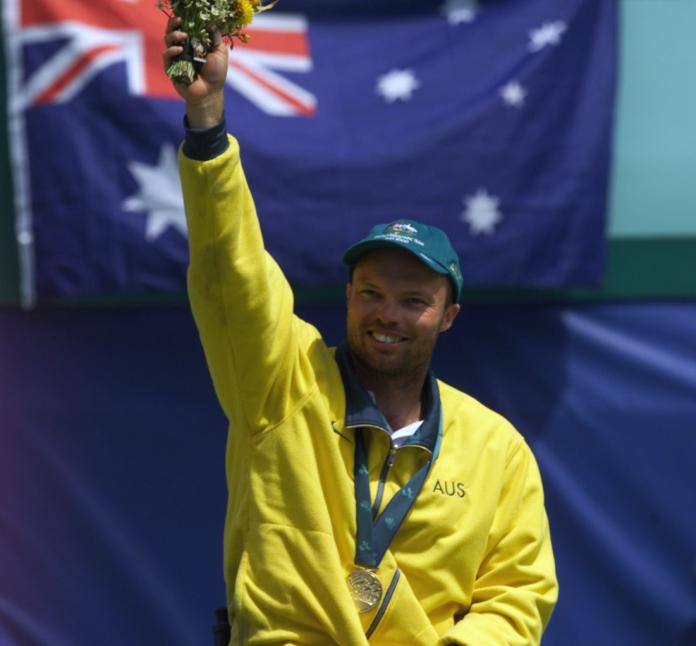 A male wheelchair tennis player celebrates on a podium - he is holding a bouquet of flowers