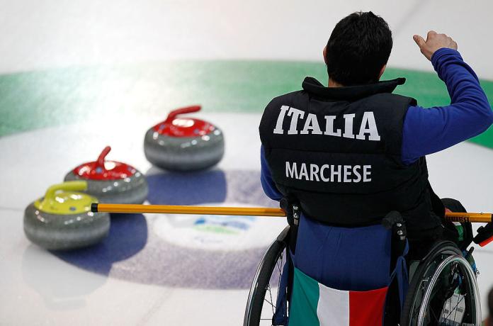 A photo of a male wheelchair curling athlete that was taken from his behind. His uniform says "Italia"