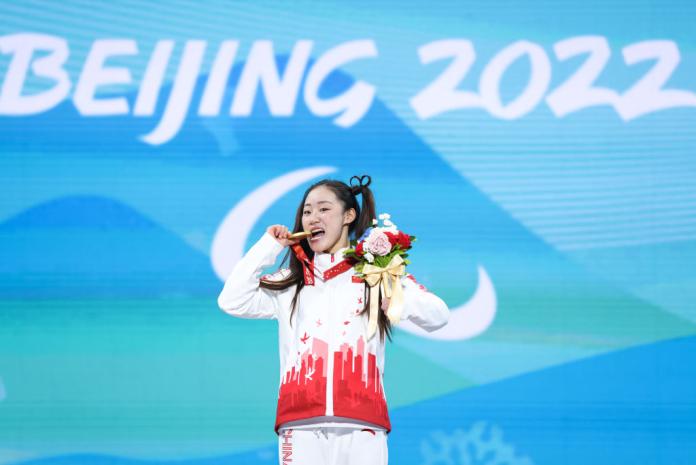 A female athlete bites her gold medal on the podium
