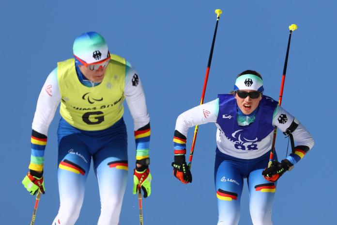 A female Paralympic skier and a sighted male guide are competing in a cross-country skiing race