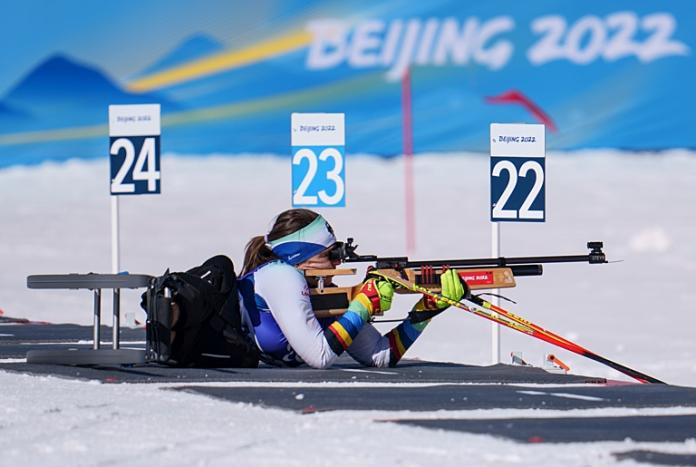 A female athlete is competing in target shooting, she is lying on the snow aiming a rifle
