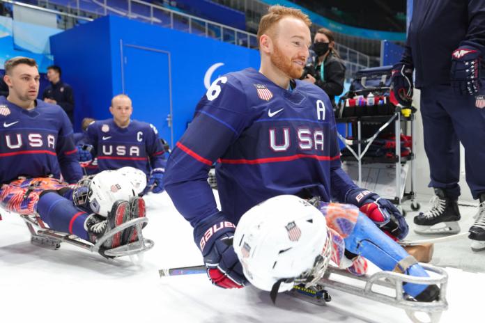 Three male Para ice hockey players line up to go onto the ice rink with their helmets off
