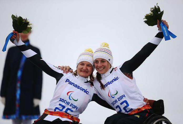 Two women in wheelchairs pose for photo with their arms around each others shoulders