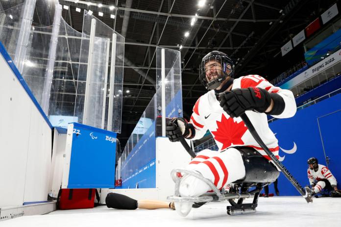 A male Para ice hockey player wearing a helmet is entering the field of play