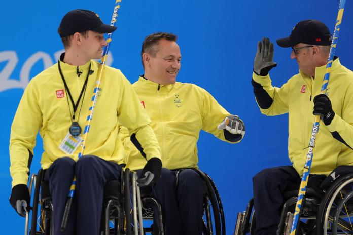 3 male wheelchair curler from team Sweden, high fiving each other