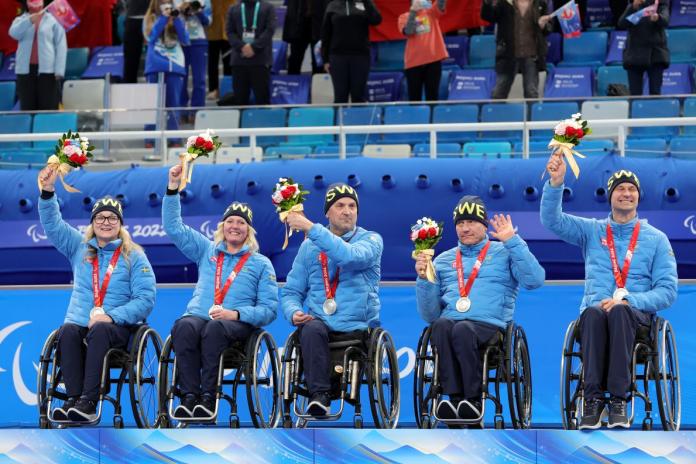 Team Sweden's five wheelchair curlers  with two females and three males celebrating silver medal while raising their flowers in the sky