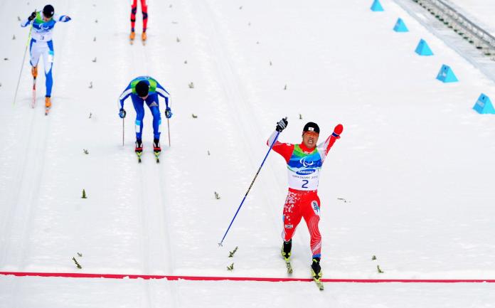 A male Para cross-country skier skiing past the finish line ahead of his opponents at the Vancouver 2010 Paralympic Winter Games 