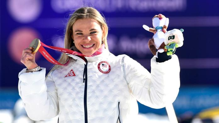 A female athlete is smiling on the podium, holding her gold medal