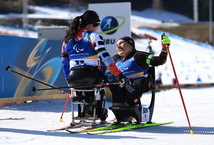 Two female sit-skiers interact on the snow