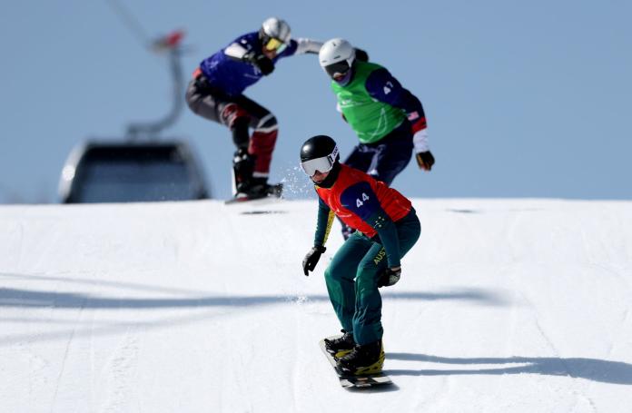 Three male Para snowboarders racing, while one of them leads