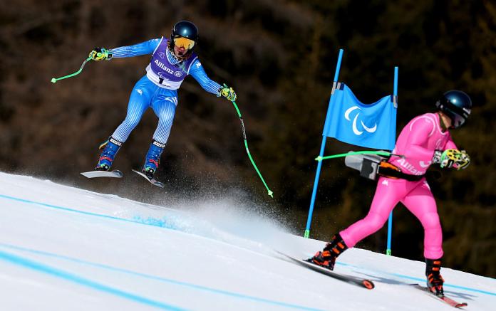 A female skier in blue follows a male guide in pink down the piste