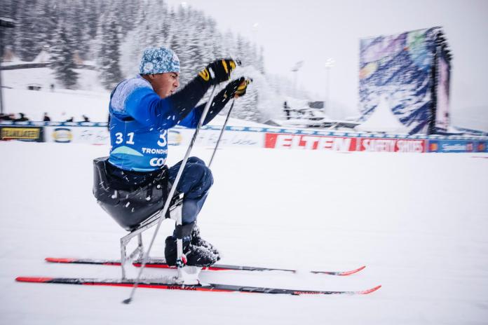 A male Para athlete going forward in sitting Para cross-country skiing while it is snowing
