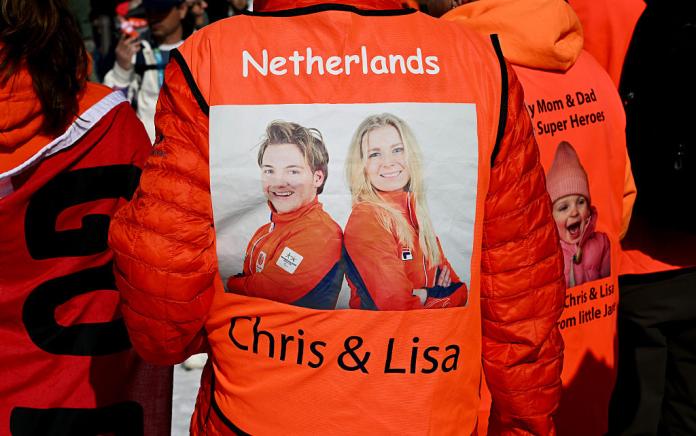The back of a person in an orange jacket displaying a photo of a man and a woman in orange
