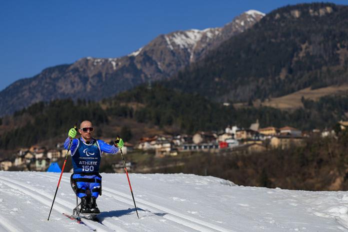 A sit-skier in blue on a cross-country course with a mountain backdrop